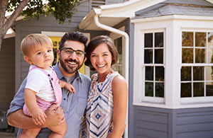 Couple with baby smiling in front of their home